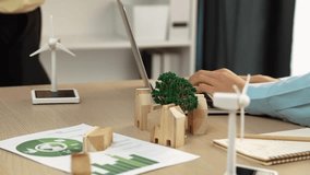 Businesswoman discussion with businessman working on laptop about green power graph. Windmill model represented using clean energy, wooden block symbolized eco house scatter on the table. Delineation. - Powered by Shutterstock - Get 15% off with code: PIKWIZARD15