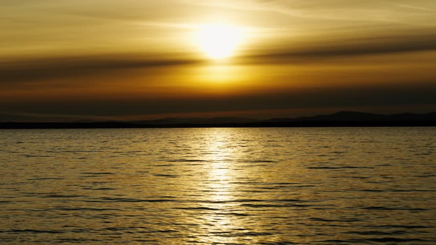 Extremely beautiful cloudy sunset on the lake. Reflection and brilliance of sunlight on the surface of the water. Natural beauty.