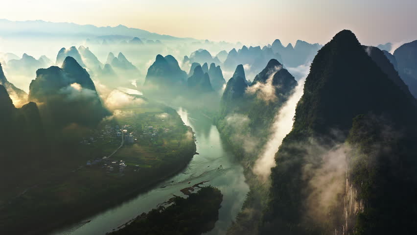 Aerial shot of the dramatic karst mountain with winding river landscape surrounded by morning fog and clouds at sunrise in Guilin, China. 