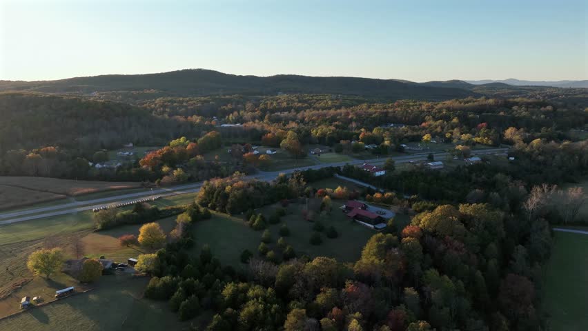 Aerial flight along American insterstate road at golden sunset in American town. Colored autumn dusk scene in blue ridge mountains. Houses and homes along main suburb road. Lateral shot.