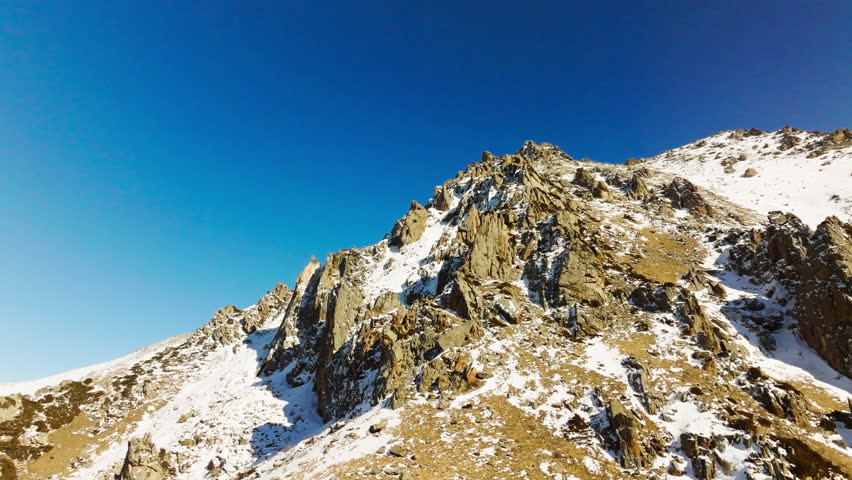 Aerial view of snow-covered mountains in Kyrgyzstan under clear blue sky at sunny winter day. Arc to the left camera movement.