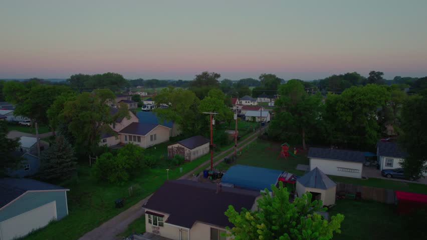 Maxwell, Nebraska neighborhood at dawn. Pastel sky, tree-lined backyards, alleys, and modest homes convey peaceful Midwestern small-town life.