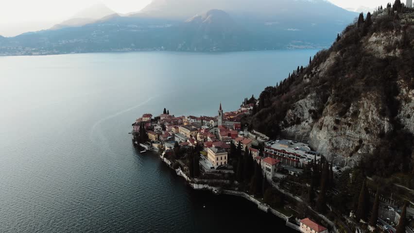 Aerial footage reveals a fog-blanketed Lake Como with silhouetted trees emerging in the serene, muted landscape. The atmosphere is tranquil, with soft, diffused lighting.