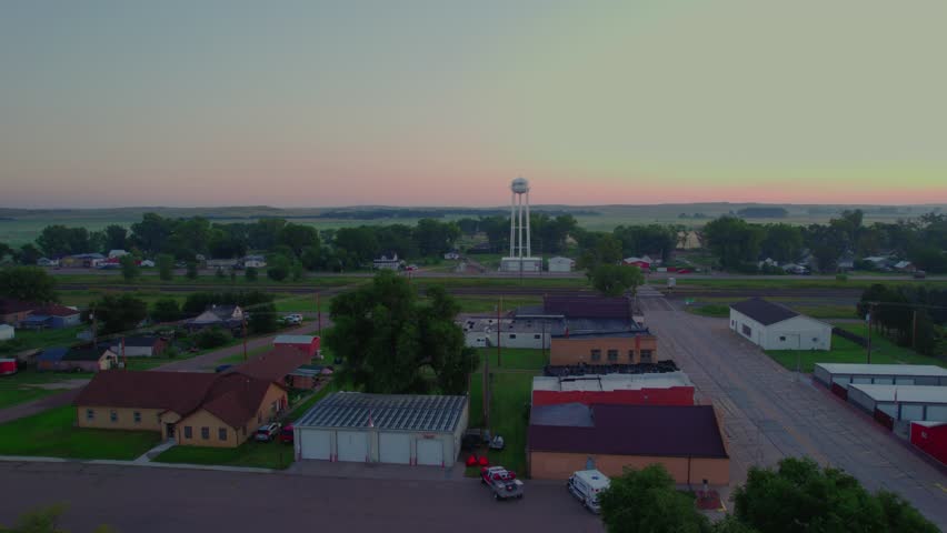 Calm drone push over Maxwell, Nebraska at first light. Water tower rises, quiet streets, rail line, and prairie horizon under soft pastel dawn, perfect Americana establishing B-roll.