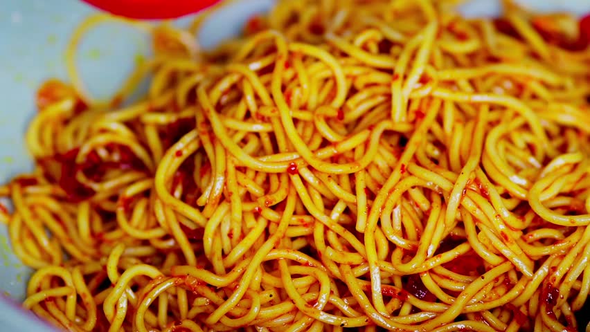 Spicy homemade fried noodles cooking in a pan, with vibrant ingredients sizzling, showing delicious home-cooked meal preparation.