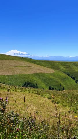 View of Elbrus from the Gumbashi pass, the highest mountain pass in Russia. View of the green mountains and hills. An epic view of the snowy peaks and valley. The North Caucasus. 4К