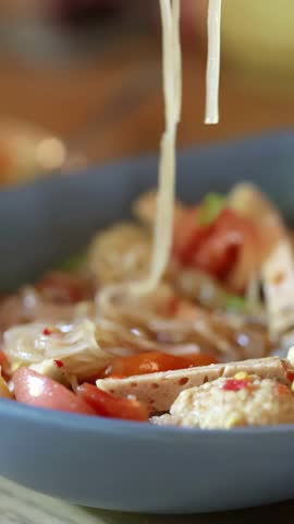 Close-up of spicy Thai noodle salad, deep fried pork skin, fork lifting food, natural lighting