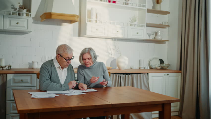 Finance and family budget, old lady and her husband counting money and spreading . Elderly married couple sitting at home kitchen and planning expenses for future month, pay mortgage and credit debts
