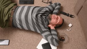A man with a beard stretches and rests while lying on the floor, viewed from above, surrounded by gadgets: a laptop, a tablet, headphones - Powered by Shutterstock - Get 15% off with code: PIKWIZARD15