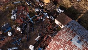 Drone video showing a cluttered scrapyard with rusted metal parts, industrial debris, an overgrown vintage bus, and an abandoned car among tall grass and scattered materials. - Powered by Shutterstock - Get 15% off with code: PIKWIZARD15