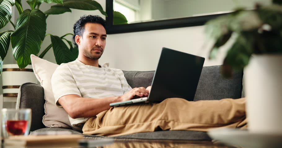 Laptop, relax and smile of man on sofa in home living room to search for streaming recommendation. Break, computer and cozy with happy person reading movie review in apartment for subscription