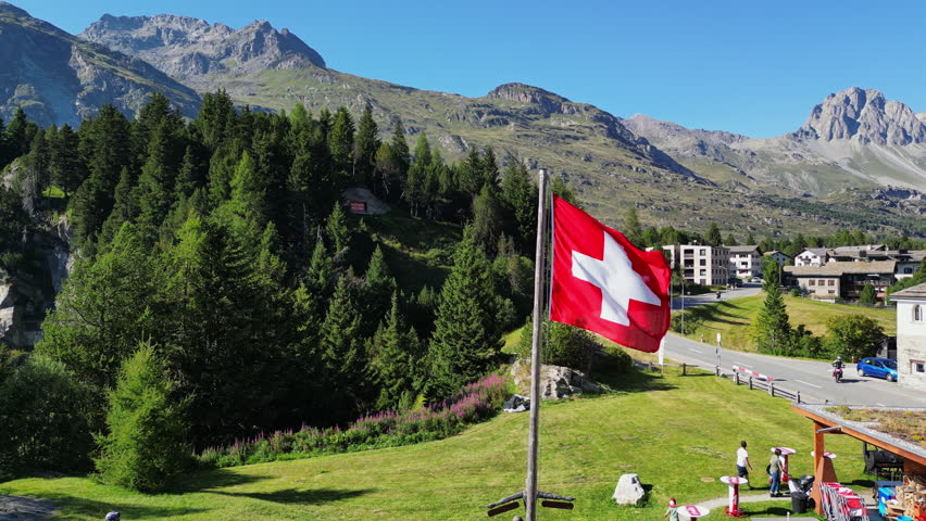Aerial view of the Swiss flag flying in the Alpine mountains. Peaks and rocky slopes of the mountains in a beautiful landscape of European nature.