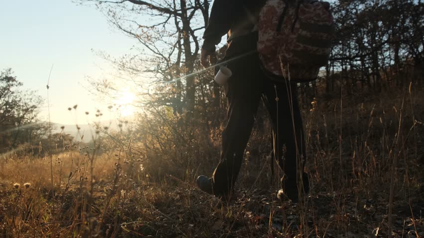 The camera follows a traveler walking energetically along a mountain road toward the sun at sunset or sunrise. Solo hiking. Tourism and survival in extreme conditions. Round the world journey on foot.