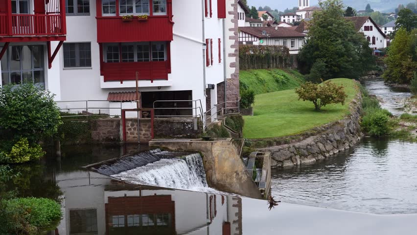 House with a red roof and a white wall. The house is next to a river. The house has a balcony