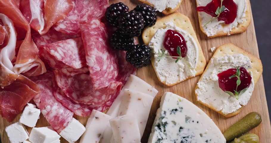 set of various meat and cheese snacks on wooden cutting board, closeup of delicatessen served for party