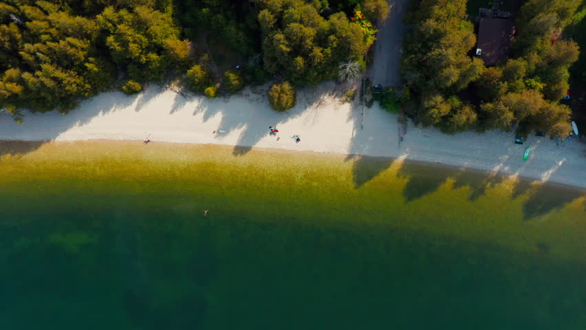 Gentle waves lap against the pale sand of Pebble Beach in Door County, Wisconsin, where forest shadows stretch toward emerald waters, creating a peaceful coastal contrast.