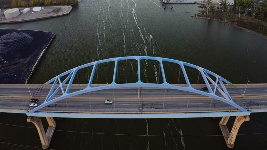 Cars move steadily across the Leo Frigo Memorial Bridge as it stretches over the calm waters of the Fox River, framed by industrial docks and soft evening light.