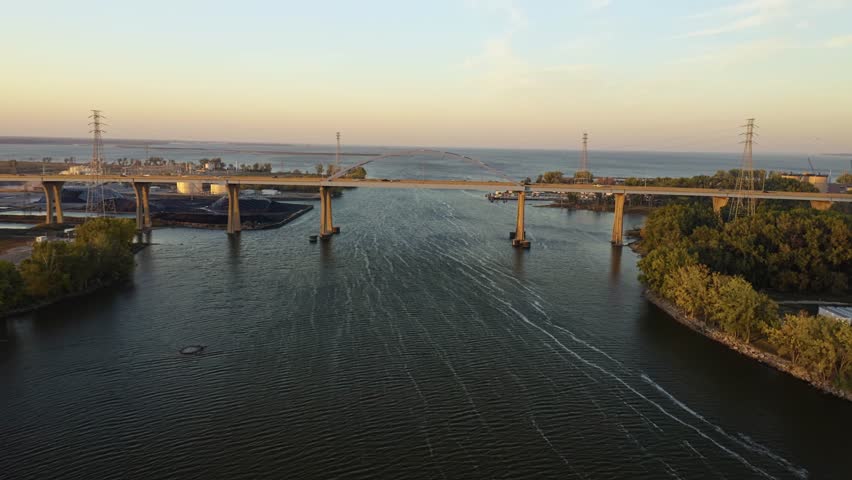 The Leo Frigo Memorial Bridge rises gracefully above the Fox River, guiding traffic toward the vast expanse of Green Bay as golden evening light reflects across calm waters and wooded banks.