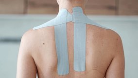 Close-up of a woman massaging her taped shoulder blades and upper back. Kinesiology taping and self-care techniques for muscle tension, pain relief and physical recovery at home - Powered by Shutterstock - Get 15% off with code: PIKWIZARD15