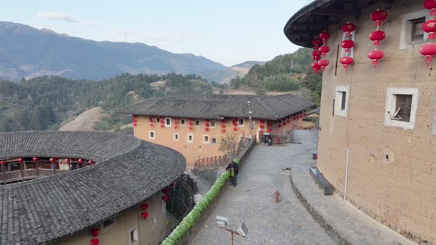 Aerial view of the earthen Tulou houses, adorned with vibrant red lanterns, contrasting against the stone pathways, Tulou, Fujiang, China.
