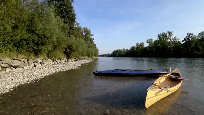 Two boats resting peacefully on the clear river water near the rocky shore line