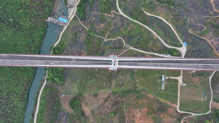 Aerial view of the long Pingtan Bridge cutting through the landscape, contrasting with lush greenery and a flowing river, Pingtan Bridge, Guizhou, China.