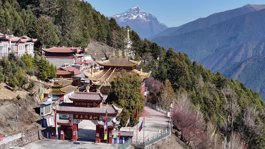 Aerial view of a traditional temple complex nestled on a lush green mountainside, with a snow-capped peak majestically rising in the background, Huaqiu, Sichuan, China.