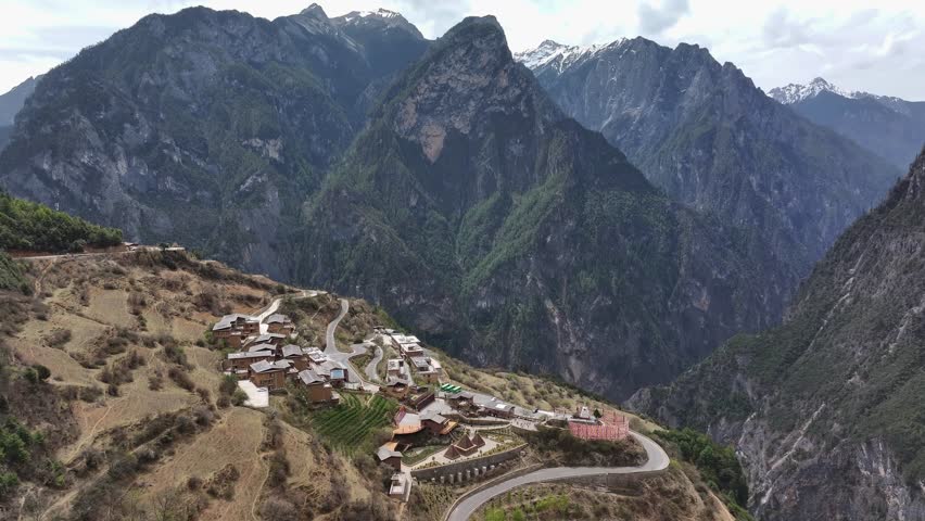 Aerial view of traditional village architecture contrasting against the rugged textures of the towering mountains, Shangri La, China.