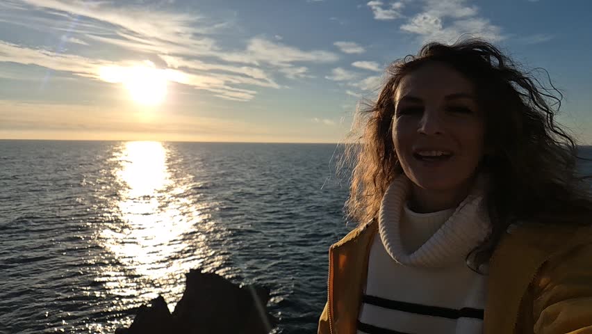 Woman ocean sunset. Traveler enjoys golden hour view from cliff edge, waving goodbye to the beautiful day.