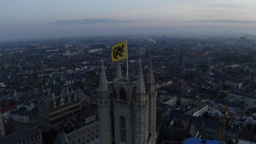Aerial view of the Belfry of Ghent topped with a vibrant flag, towering over the city