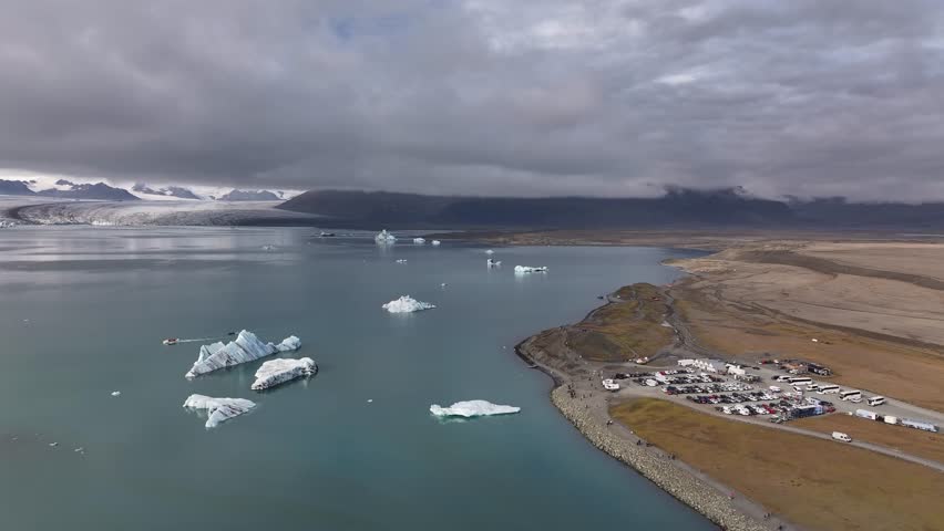 Wide drone view of Jökulsárlón lagoon with floating icebergs, car park and visitor area near Diamond Beach, Iceland.