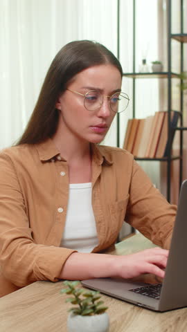 Young woman sitting at home table removes glasses rubs tired eyes after a heavy long laptop work session. Caucasian girl feels physical strain blinking rapidly and seeking rest to ease discomfort now.