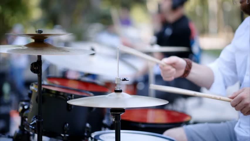 Energetic close-up of a man playing red drums outdoors, capturing rhythmic movement, vibrant color, and the passion of live street music performance.