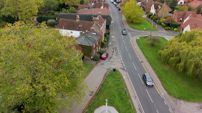Aerial establishing shot in Roydon, Essex. The drone rises slowly from the bottom of the hill, looking forward and down over the main village road, revealing houses, trees, and grass as it ascends.