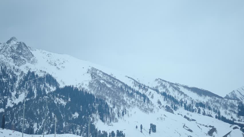 4K Landscape shot of snowy Himalayan mountain peaks during a winter storm as seen from Sonmarg in Jammu and Kashmir, India. Scenic view of snow clad mountain peaks with pine trees on top of them. 