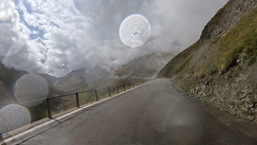 Cinematic view of a winding mountain road in the Swiss Alps on a cloudy day. Scenic alpine landscape with fog, mist, and dramatic clouds over rocky peaks