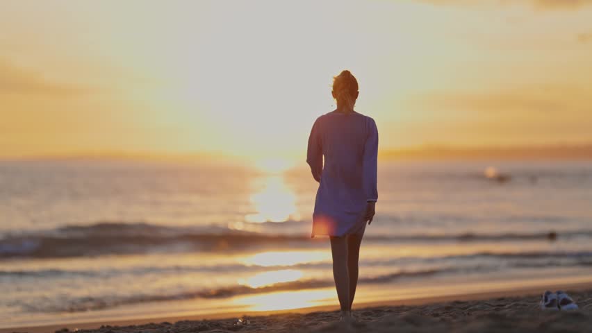 Silhouette of a woman walking on a beach at sunset