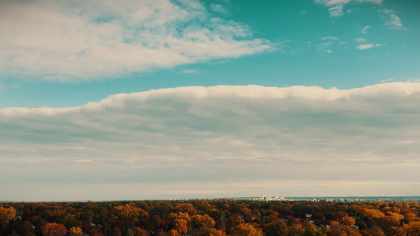 High-altitude aerial of Green Bay, Wisconsin skyline and Lambeau area framed by vibrant autumn forest canopy under a unique cloudscape