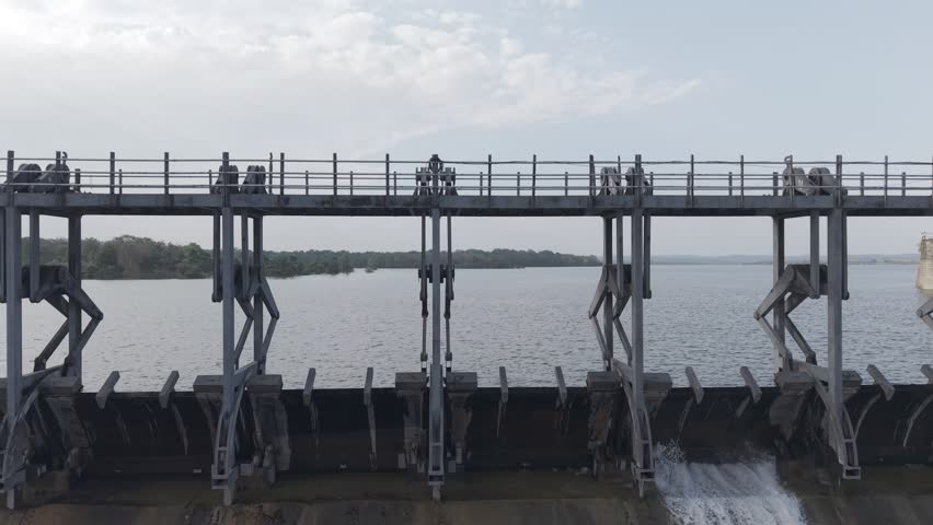 A breathtaking aerial view of a large dam and surrounding landscape, captured with a drone in cinematic dolly zoom style. The shot dramatically highlights the vast scale of the dam and the flowing wat
