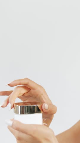 A woman opens a cream jar enjoying the lovely scent while admiring the product in natural light