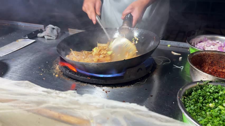 Making stir fried rice noodles on a street food cart at night in Southeast Asia