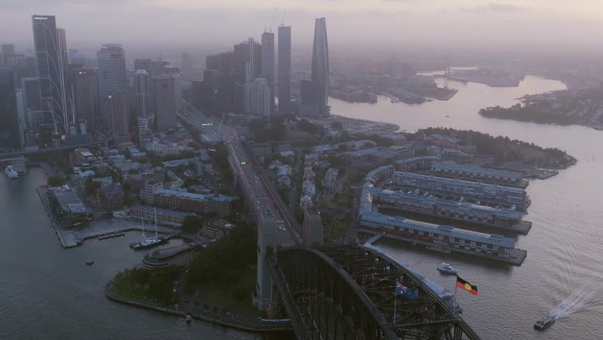 Aerial view over Harbour Bridge and away from the Sydney skyline, hazy dusk