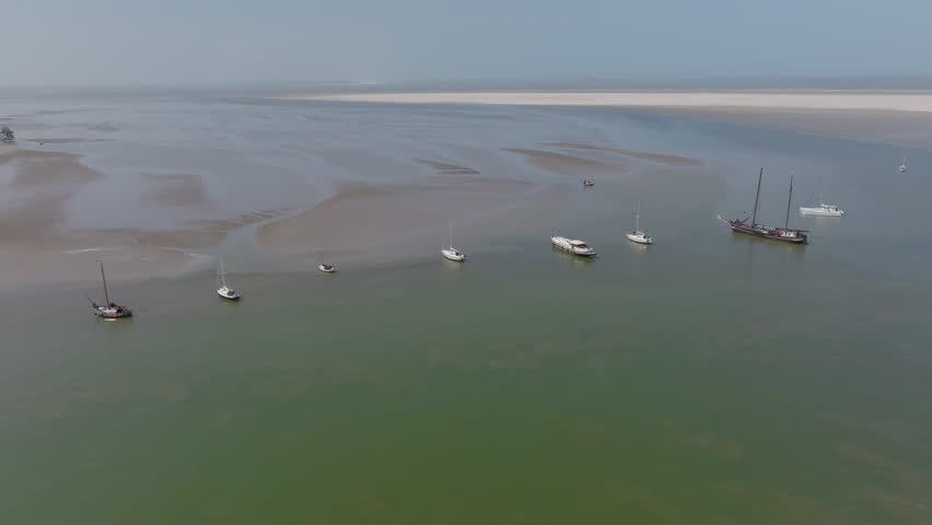 Oblique wide view of boats near patterned sandbanks and green water at low tide; yachts, catamaran and a motor barge present. Wadden Sea.