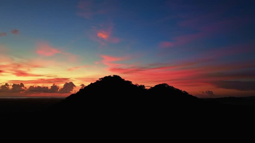 A beautiful panoramic sunset on a tropical mountainous coastline. Red clouds in the evening blue sky. A vibrant sea sunset over the coast. An exotic view of nature at dusk.