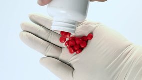 Red pills poured from a bottle into a gloved hand on white background, showing the large amount of medicine needed to maintain good health. - Powered by Shutterstock - Get 15% off with code: PIKWIZARD15