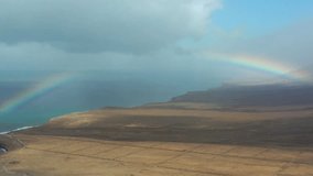 Natural landscape in Fuerteventura, Canary Islands  a dirt path through arid land facing the sea, with a colorful rainbow breaking through dramatic clouds. - Powered by Shutterstock - Get 15% off with code: PIKWIZARD15