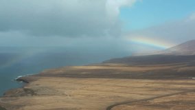 Natural landscape in Fuerteventura, Canary Islands  a dirt path through arid land facing the sea, with a colorful rainbow breaking through dramatic clouds. - Powered by Shutterstock - Get 15% off with code: PIKWIZARD15