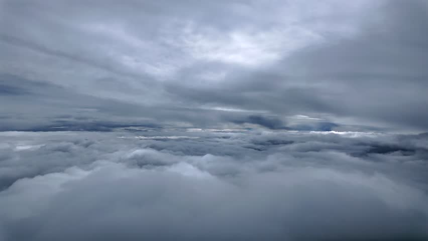 An immersive pilot’s perspective from the cockpit of a jet airplane flying between layers of threatening and darkening stratus clouds in a dramatic sky.