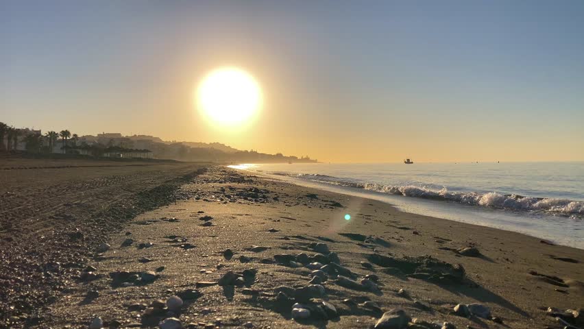 Stunning sunset illuminates the beach and rocky coastline near the “El Cantal” tunnels in Rincon de la Victoria, Spain, painting the sky in warm golden hues.