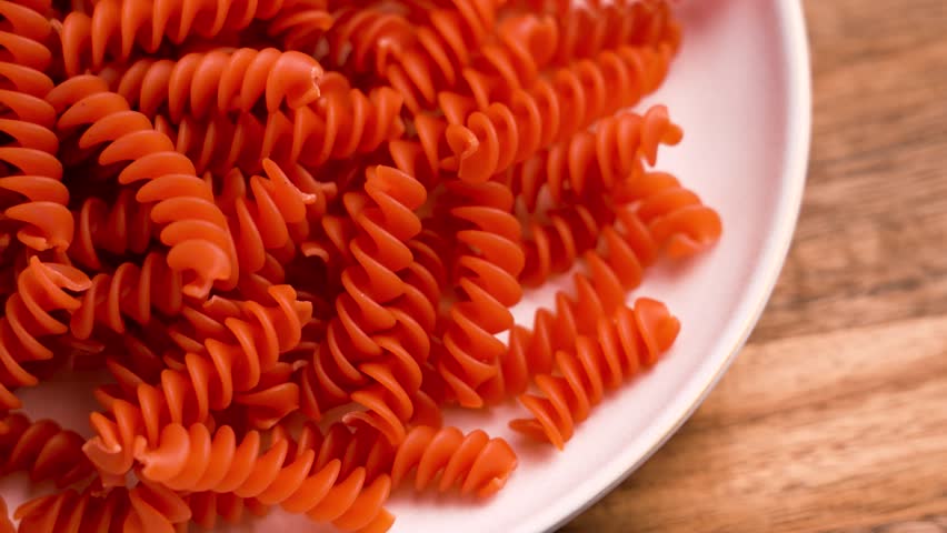 Orange lentil uncooked pasta in ceramic plate on wooden table close up